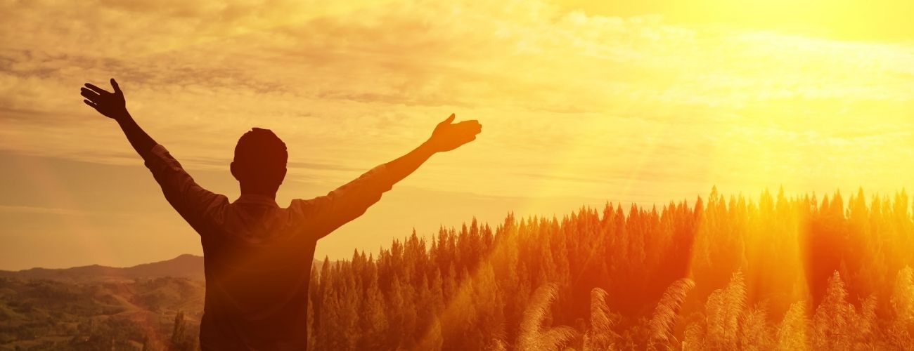 Young man in field with hands raised at sunset