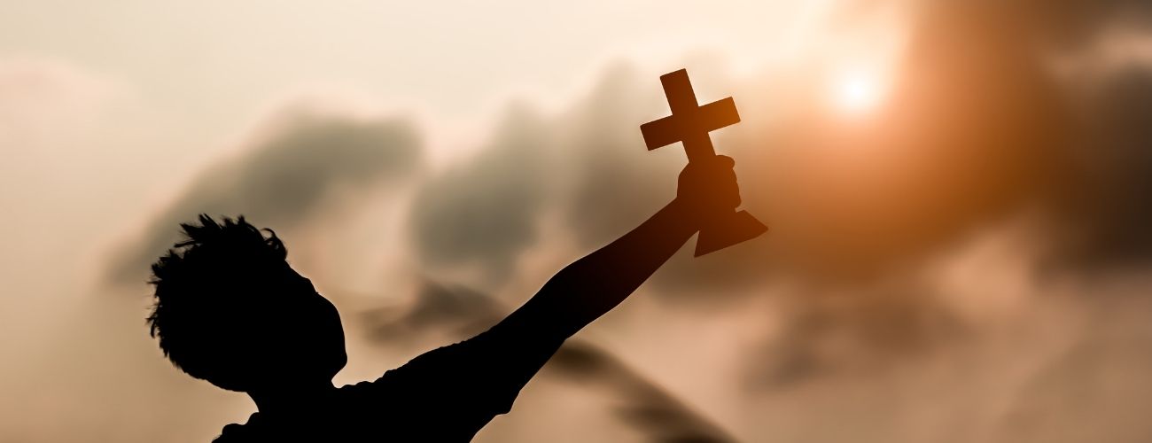 young boy holding cross in sunset background